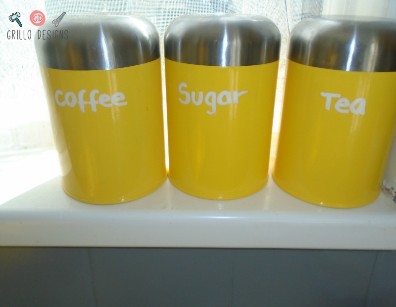 Close up view of three yellow and stainless steel canisters for coffee, sugar and tea