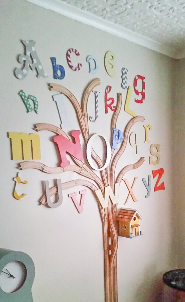 Image of a finished wooden train track made into a tree trunk with branches, with wooden alphabet shapes used as the leaves of the tree