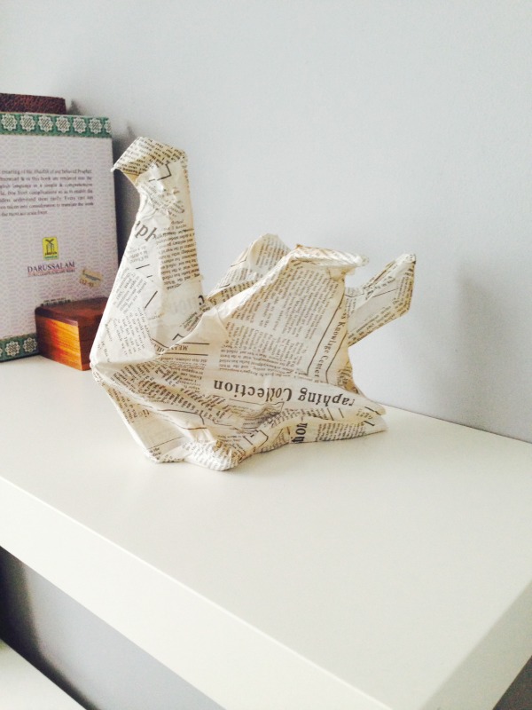 Close up image of an origami bird sculpture in newsprint on the Ikea Lack shelves.