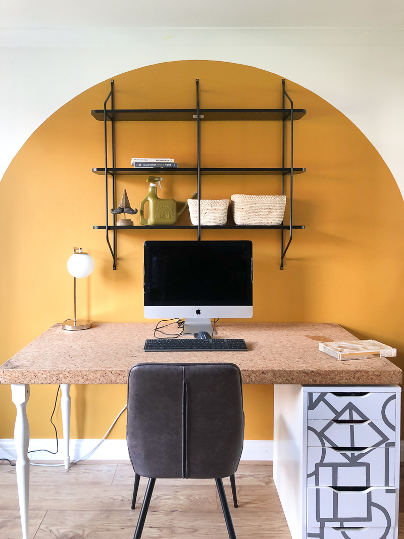 Black shelf secured to top of arch above the cork desk with computer 