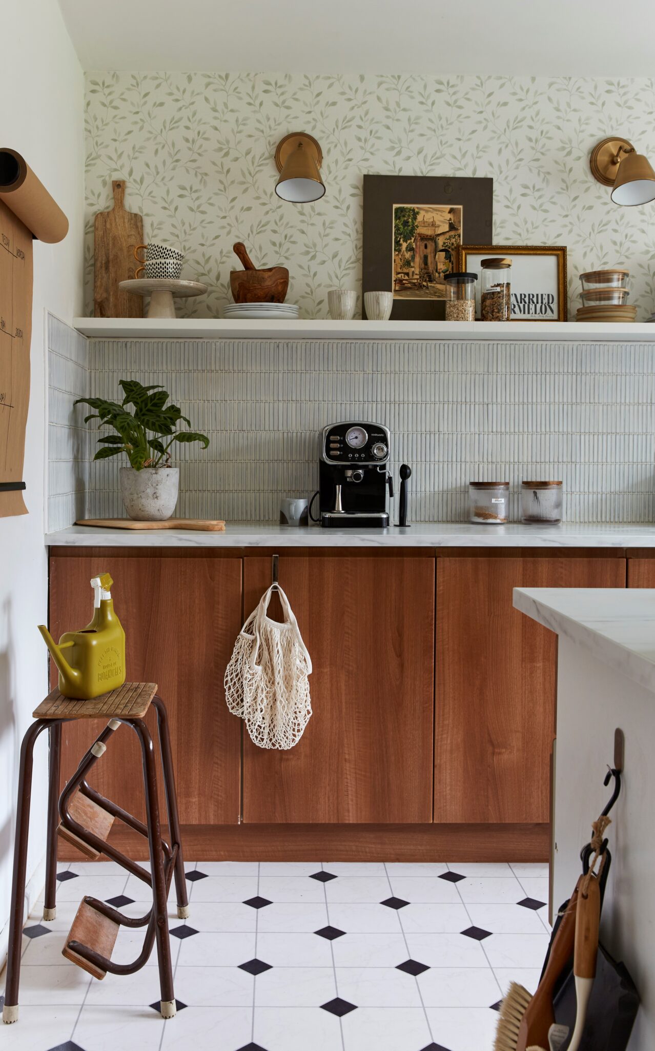 Open shelving above base cabinets with wall paper above the shelf and tile backsplash below and sconces above the shelf.