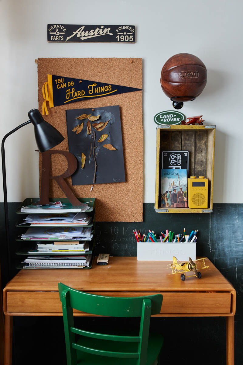 Desk area in boy's bedroom with cork board and desk top storage for pens and markers with a stack of books and green chair