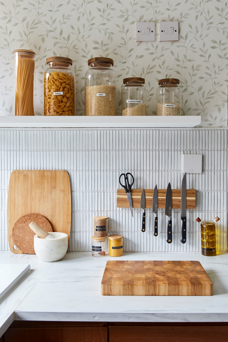 Glass jars of pasta and flour on open shelving above tile backsplash and white kitchen counter