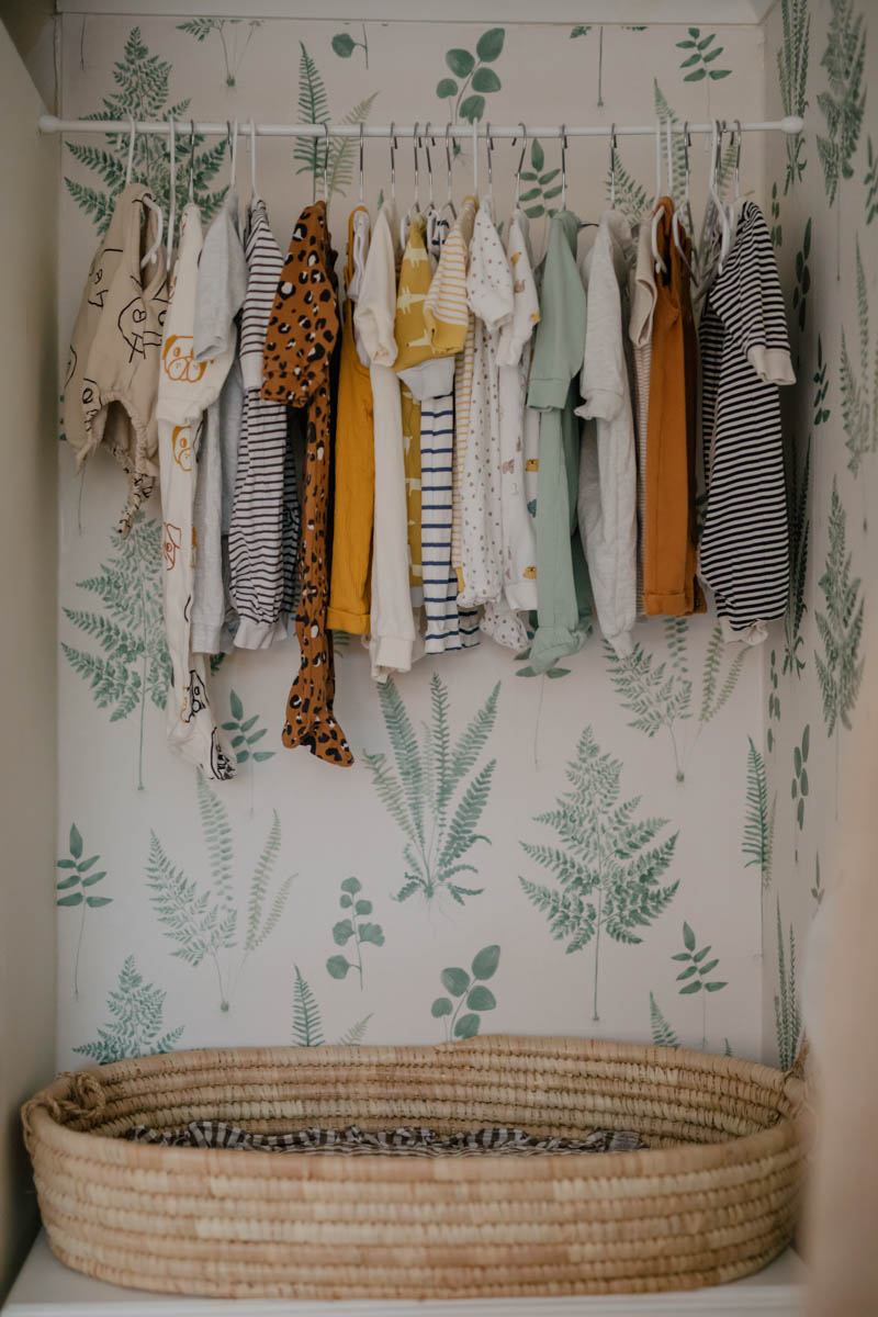 baby clothes hanging on rod above dresser in alcove
