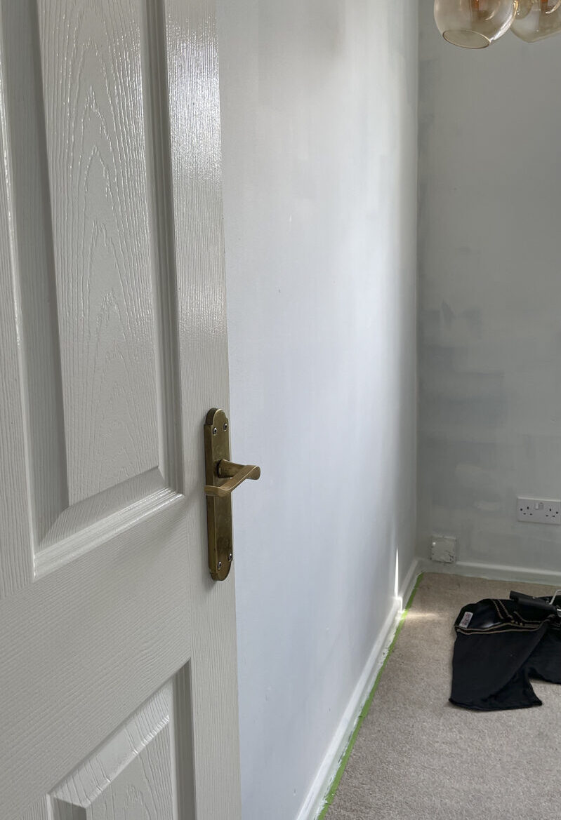 the black walls are painted over with white before the half wall of yellow is painted. a light fixture which is round bauble style glass in a trio can be seen and a white door 