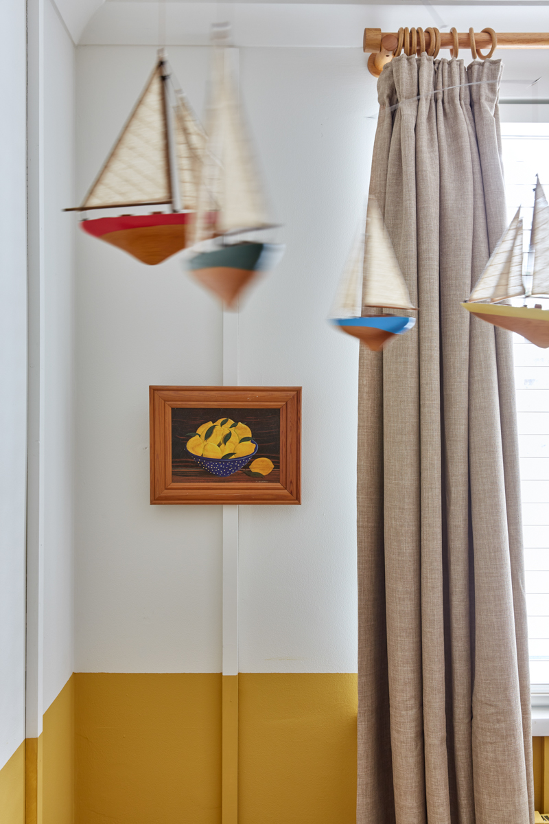 A vintage painting of lemons in a bowl hangs behind the cot on the wall next to the window. 