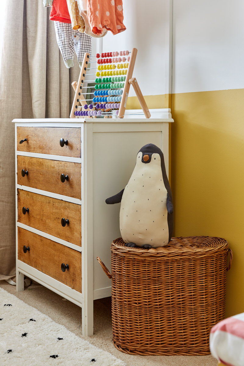 A closer look at the chest of drawers from the side, a big penguin toy sits atop a vintage wicker basket. 