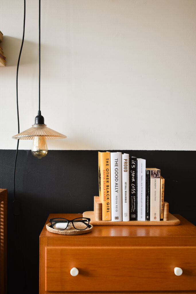ikea stolthet styled upside down on a bedside table as bookends. 6 books nestle in perfectly and a vintage style lighting fixture hangs low on a half painted black wall